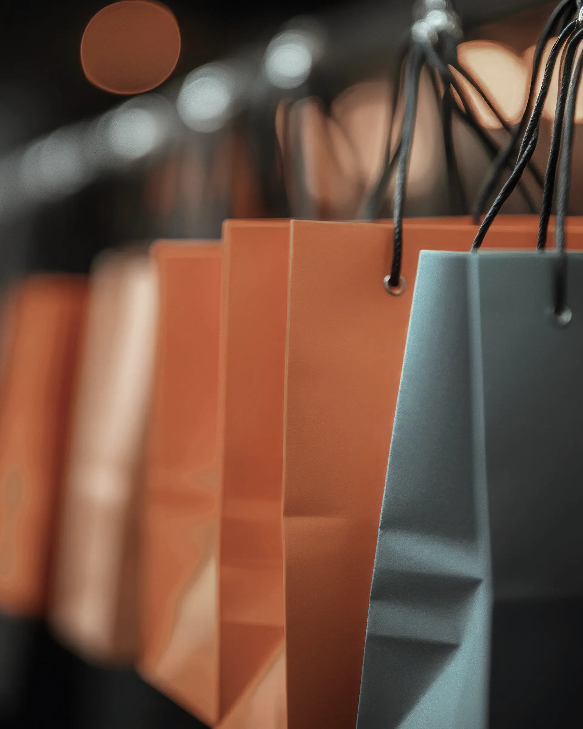 Borse per lo shopping in carta kraft arancione e blu appese in fila, simbolo di acquisti sostenibili e moda responsabile